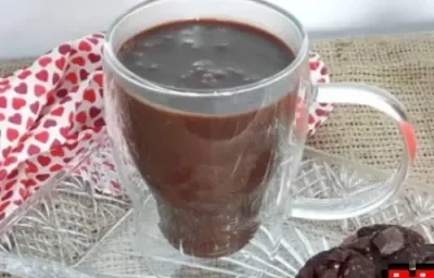 Foto da receita de Chocolate Quente. Observa-se uma xícara branca transparente com a bebida dentro, sobre um pires transparente de vidro.