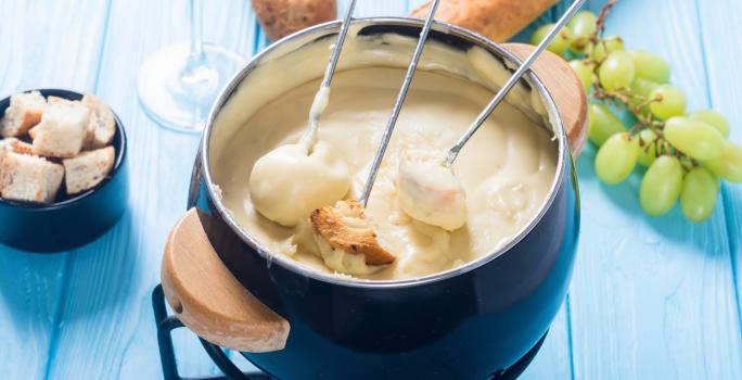 Foto da Receita de Fondue de Queijo Sem Lactose. Observa-se uma panelinha de fondue azul com três espátulas de pão dentro.