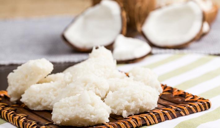 Foto da receita de Cocada Zero Lactose. Observa-se as cocadas dispostas em uma tábua e atrás é possível ver os cocos abertos.